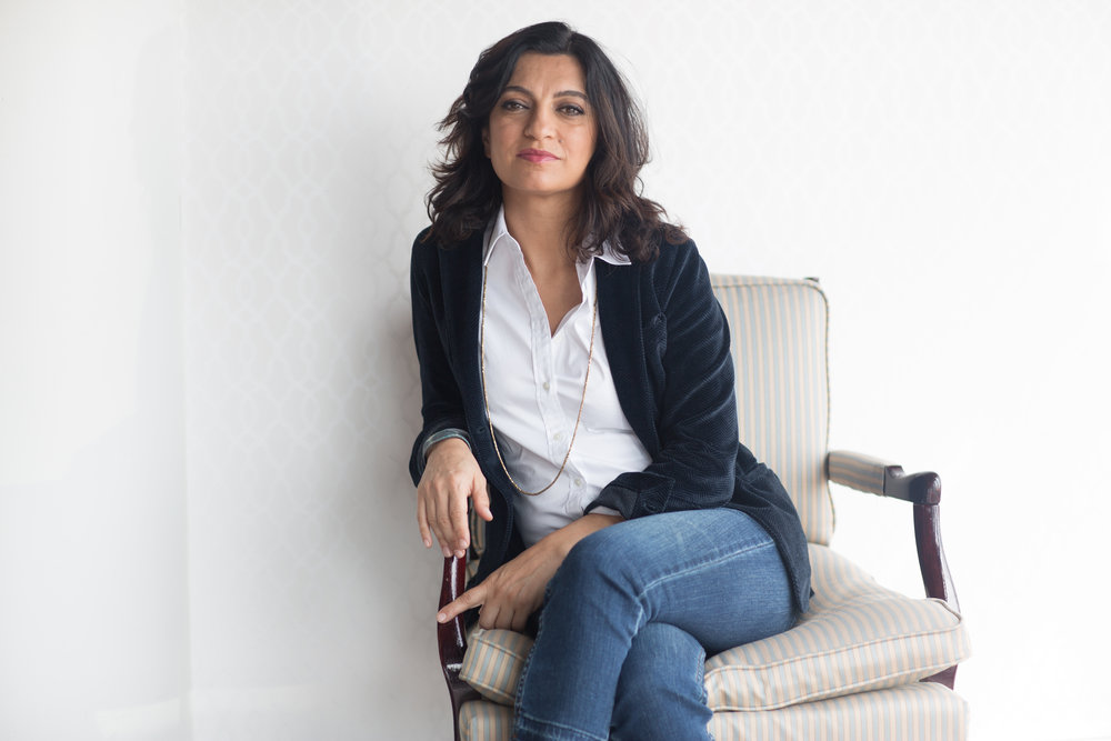 Photograph of Firuzeh Mahmoudi sitting in a chair with a white shirt, black jacket, and blue jeans