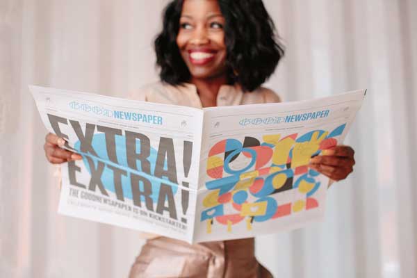 Woman holds a Goodnewspaper and smiles