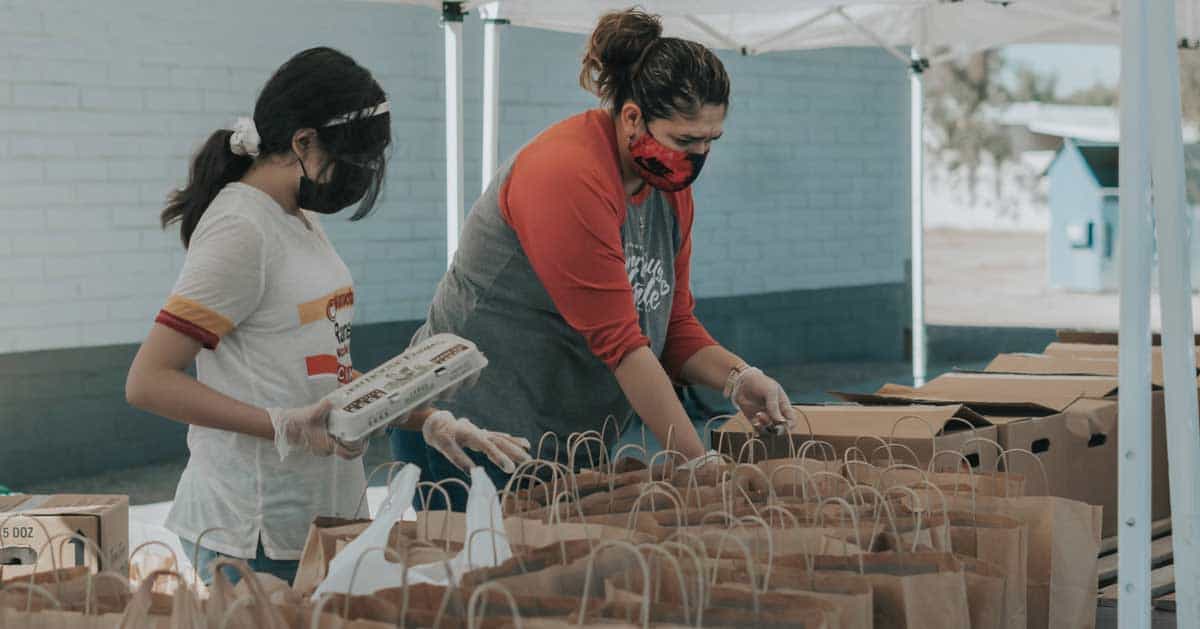Two women volunteering by packing brown bags of food