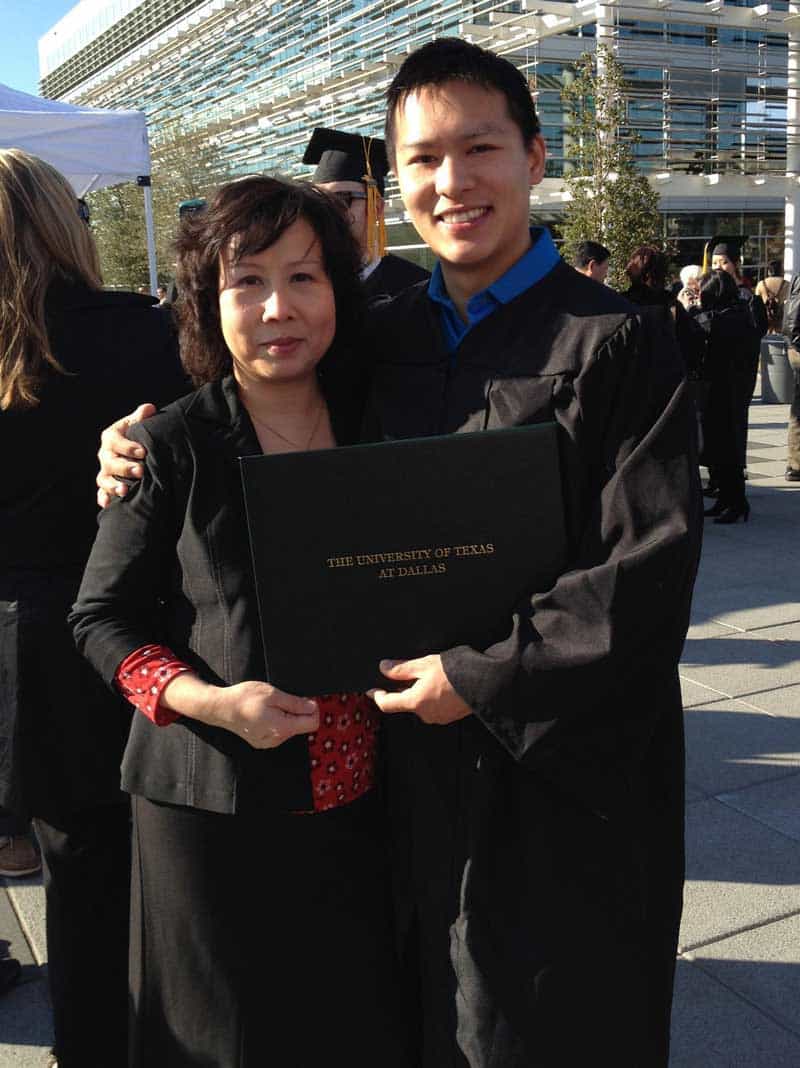 Jason Wang with his mother posing outdoors in a cap and gown while holding a degree that says The University of Texas at Dallas