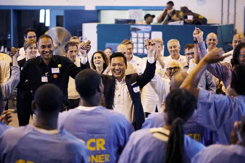 Jason Wang in a suit in a prison, raising his arms in celebration while smiling