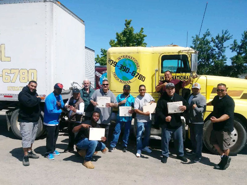Men pose with certificates in front of a yellow semitruck