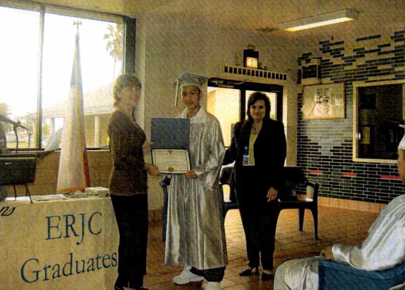 Jason Wang posing with his degree while wearing a silver cap and gown in prison
