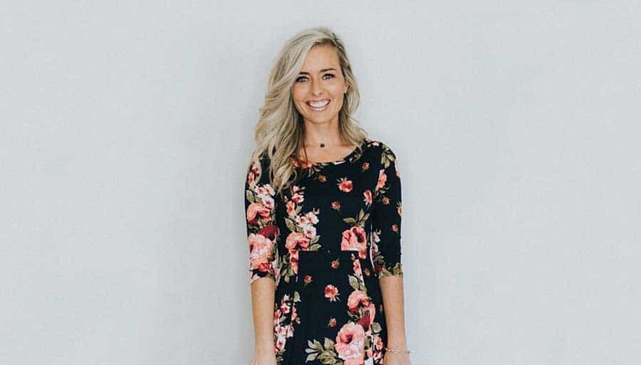 Ashely LeMieux in a floral dress smiling in front of a gray backdrop