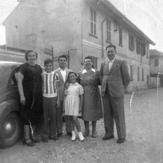 A vintage portrait of adults and children posing in front of an old car and house