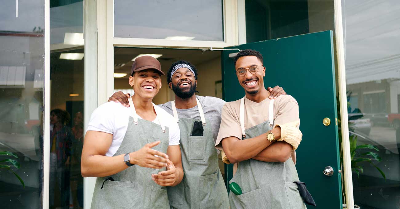 Portrait of a male group of Black happy small business workers laughing at the door of a urban plant nursery wearing aprons