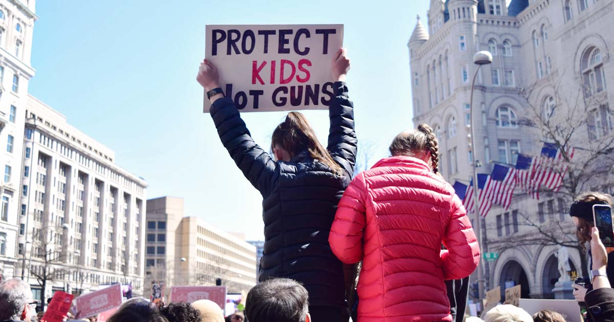 A girl stands in a crowd holding a sign that says "Protect Kids. Not Guns"
