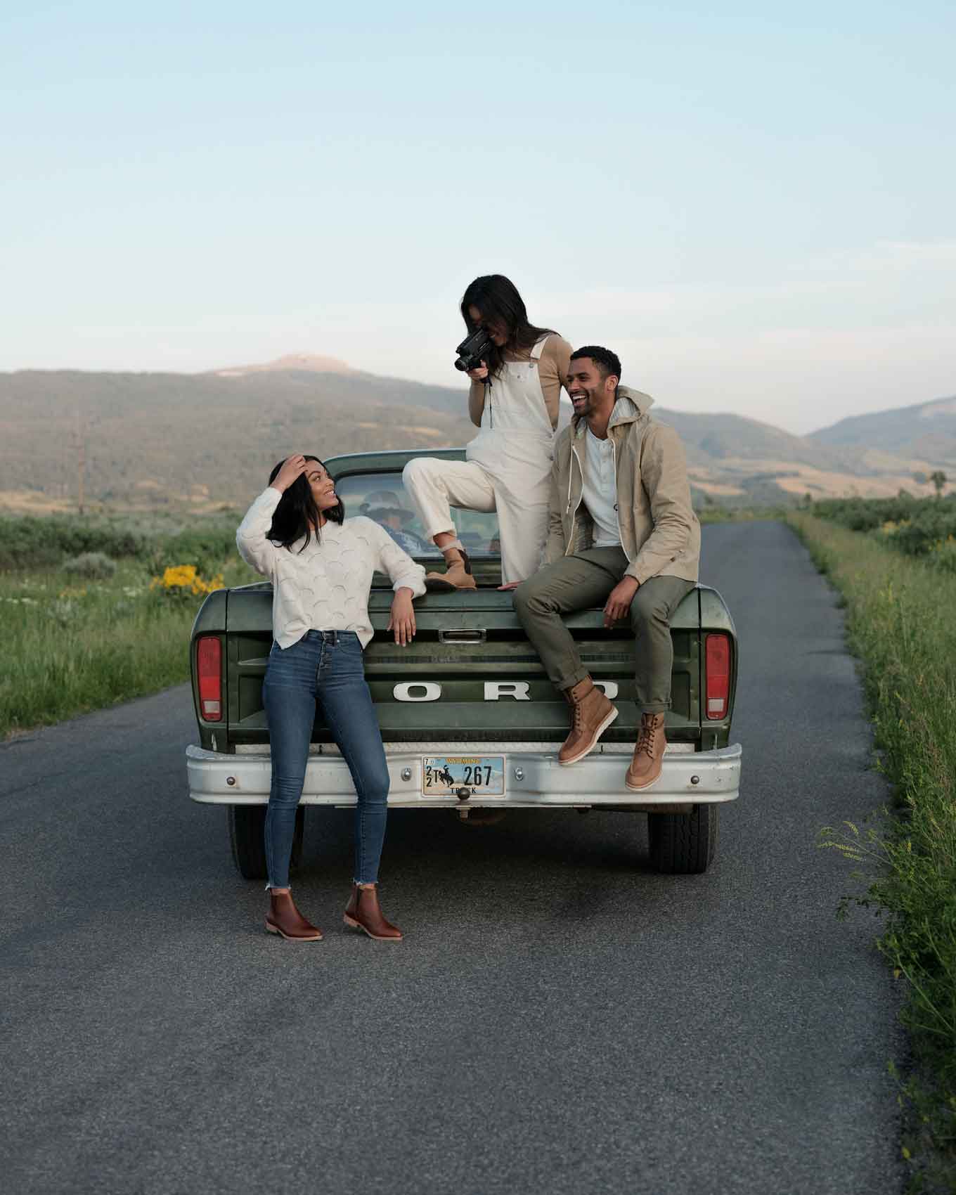 Two women and a man pose and take photos of each other on a back of a vintage truck on a country road, wearing ethically made clothes and shoes from Nisoloo