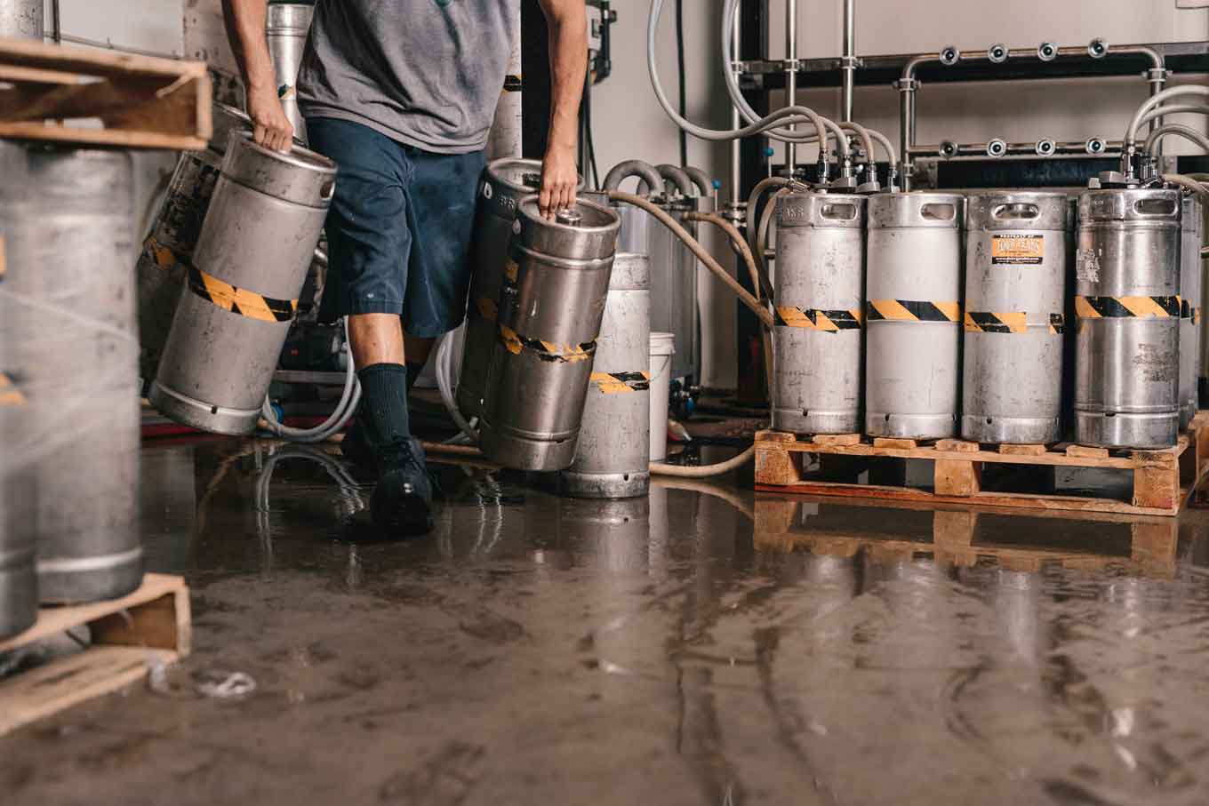 A brewery worker carrying tanks in an industrial brewery.