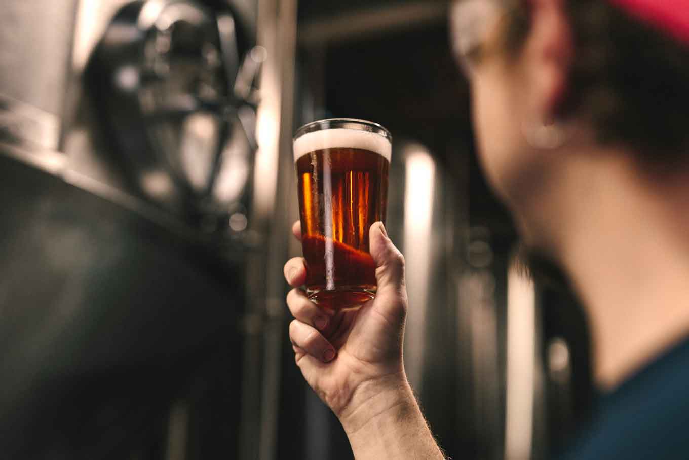 A brewery worker holding a dark beer inside of a brewery