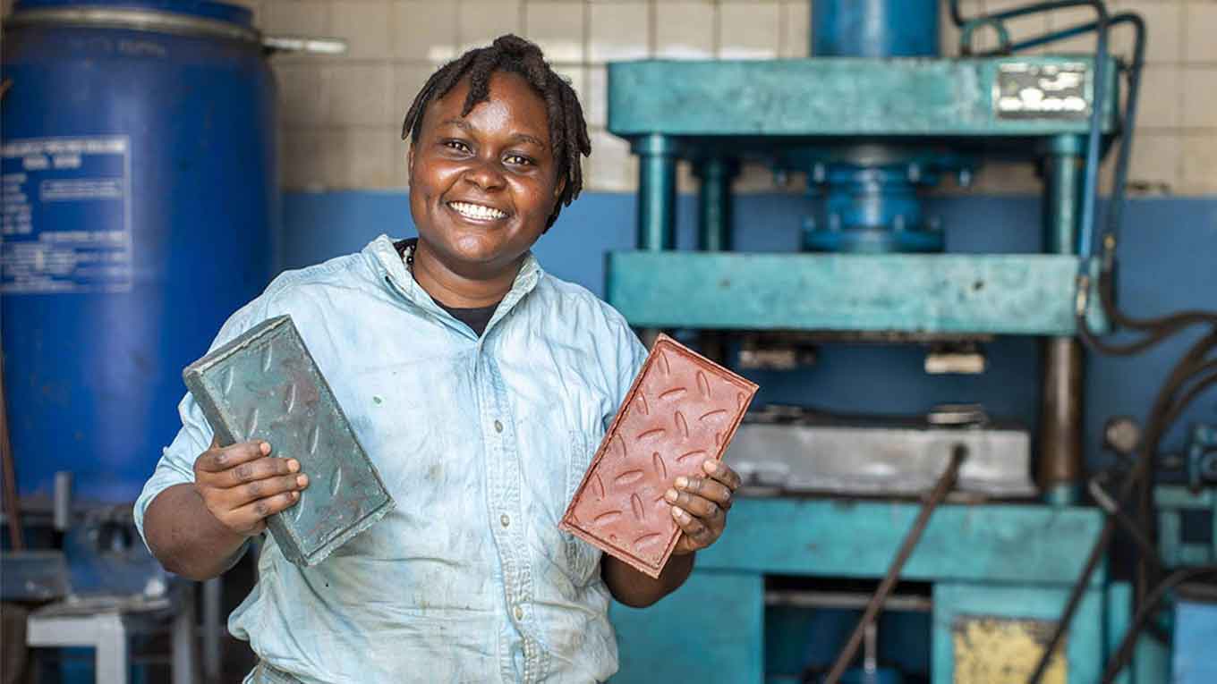 Kenyan woman smiling and holding colorful bricks made from recycled plastic