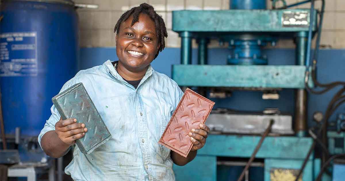 A Kenyan woman smiles and holds her recycled plastic bricks