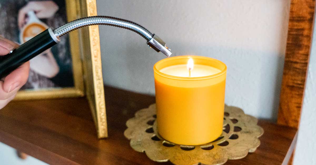 A rechargeable electric lighter lighting a yellow candle on a shelf