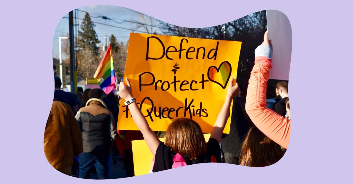 A young person holds a protest sign that says "defend and protect queer kids." 