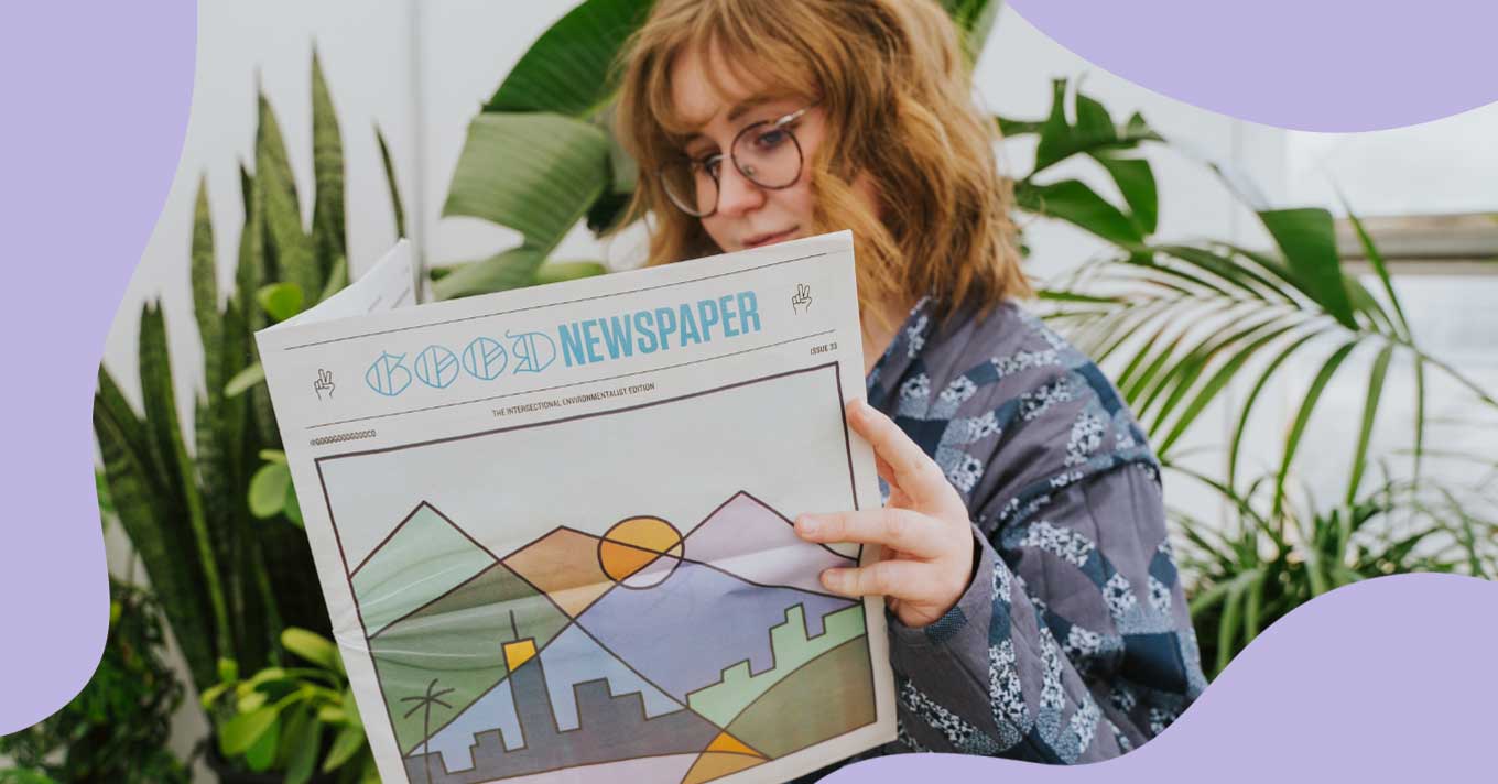 A white woman with shoulder-length blonde hair wears glasses and a blue jacket as she reads an issue of the Goodnewspaper.