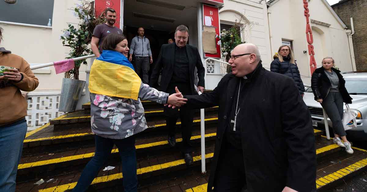 A priest welcoming a refugee wearing a Ukrainian flag