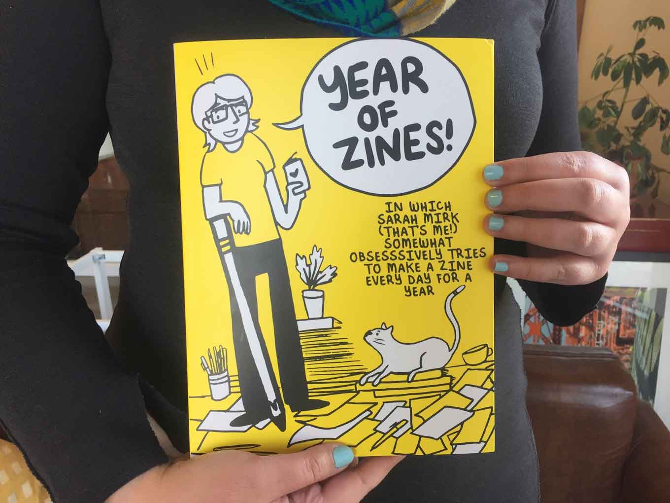 Someone holds up a copy of Sarah Mirk's book: "A Year of Zines"