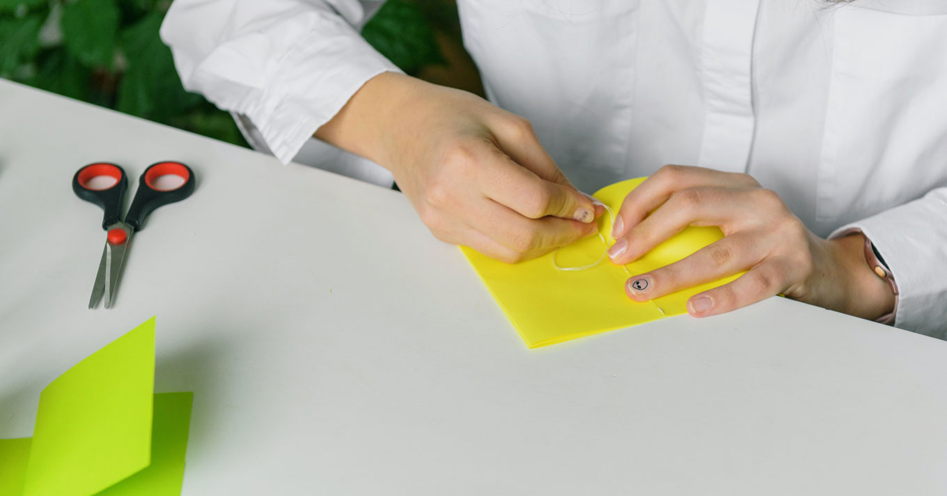 A person in a white shirt creates a zine with yellow and green paper. A pair of scissors sits atop their workspace.