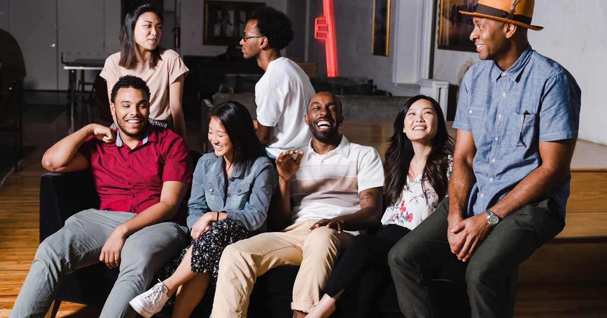 A group of Black, Asian, and Latinx friends smile and laugh on a couch in a diverse stock photo from TONL