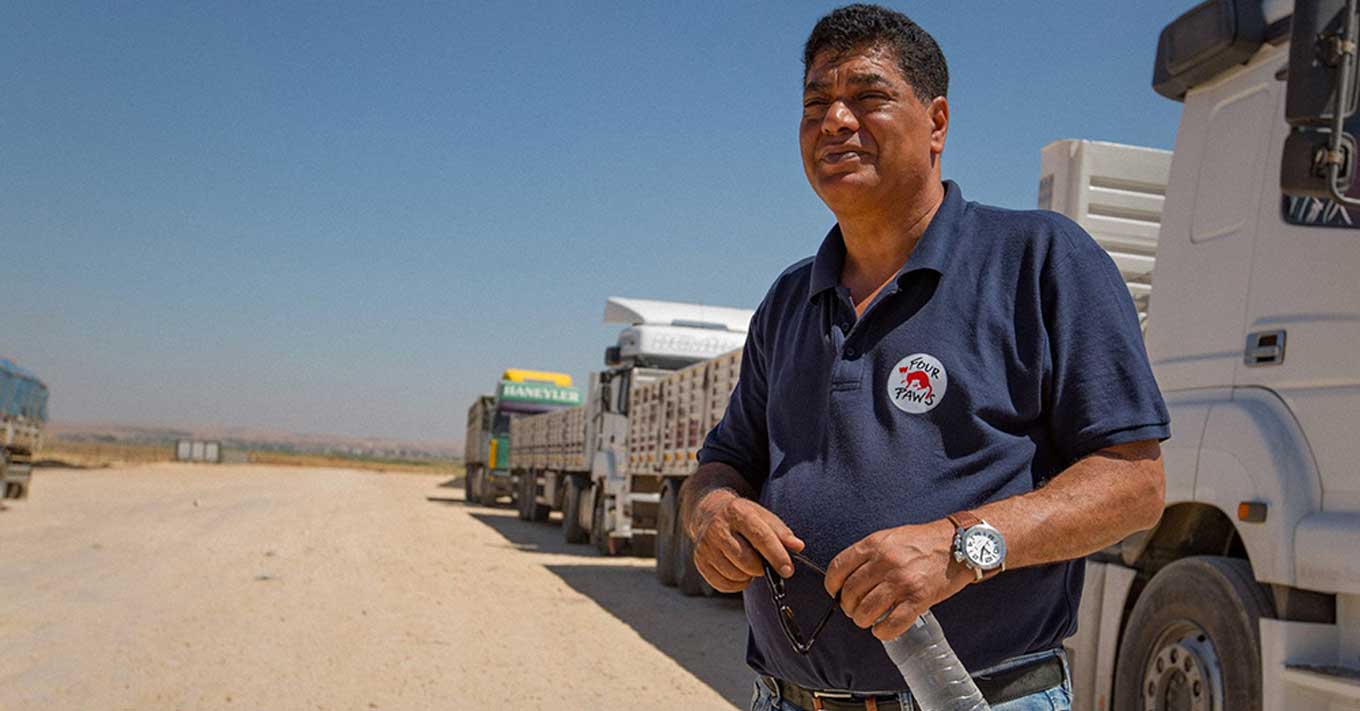 Amir Khalil, standing in front of vehicles in the desert, wearing a Four Paws International polo shirt and holding a bottle of water