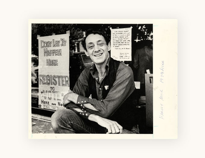Harvey Milk smiling in front of a campaign sign: Don't Let It Happen Here Register to Vote