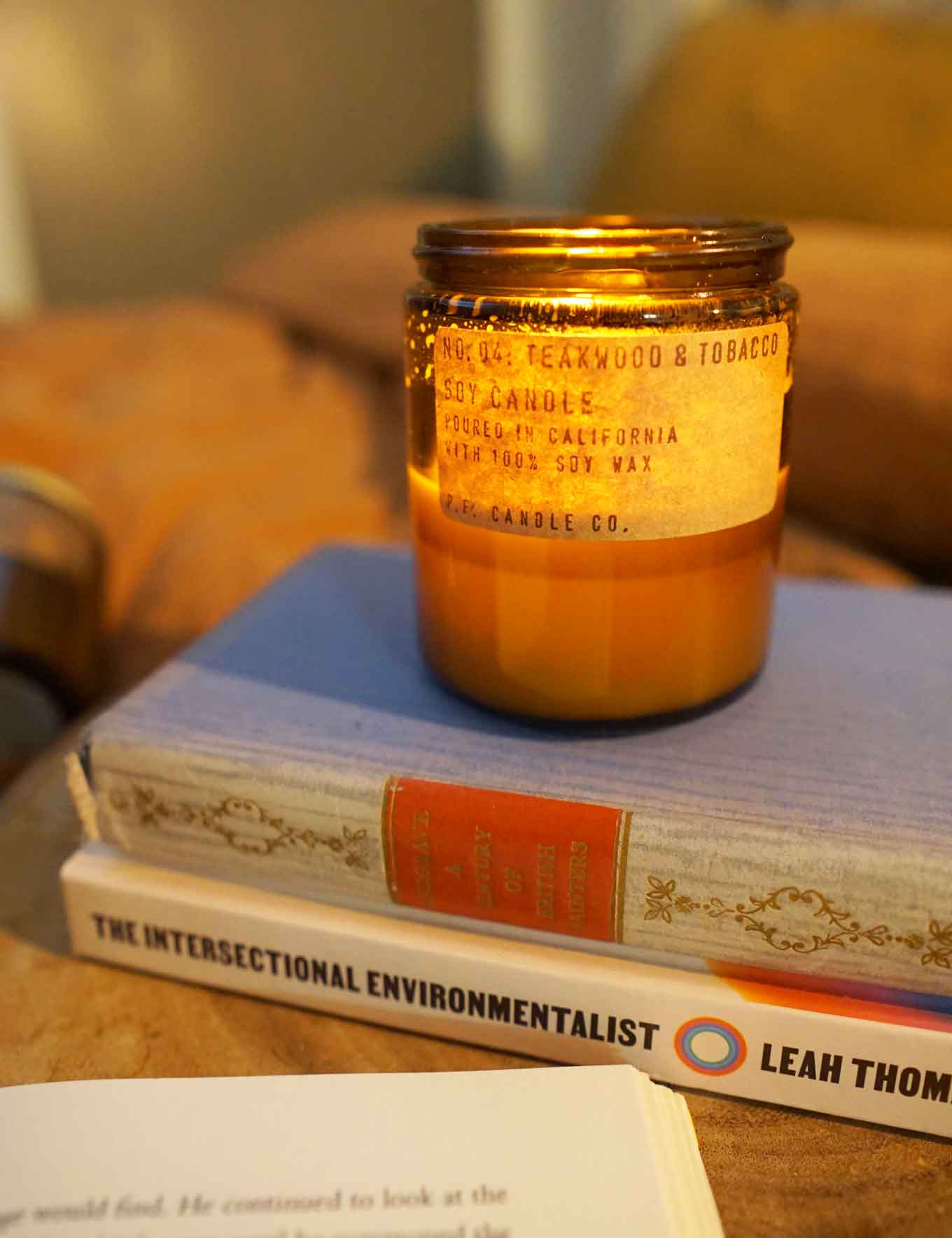 Lit candle with a label that says No 04: Teakwood & Tobacco, Soy Candle, Poured in California with 100% soy wax, P.F. Candle Co