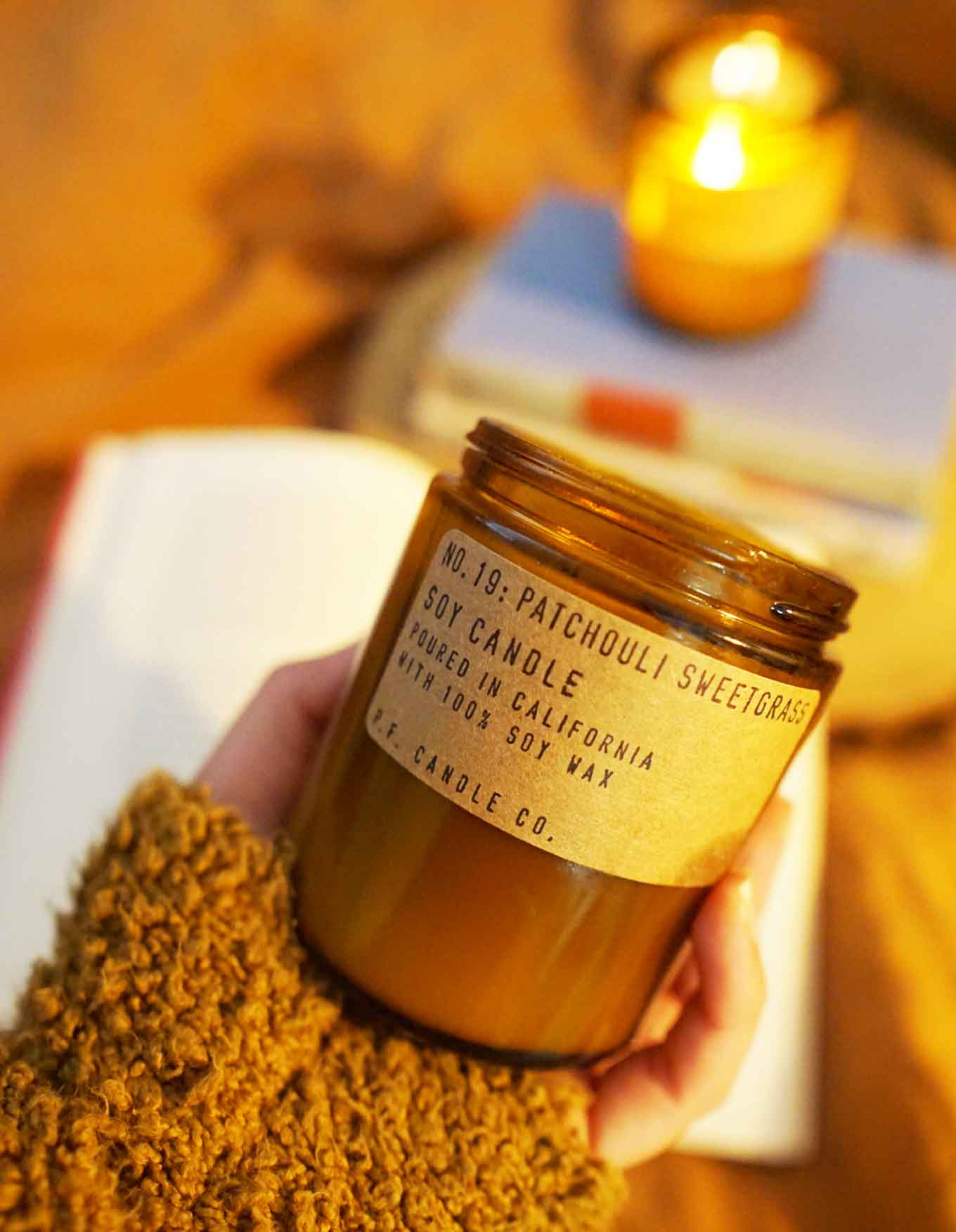 Hand holding a new candle with a label that says No 04: Teakwood & Tobacco, Soy Candle, Poured in California with 100% soy wax, P.F. Candle Co