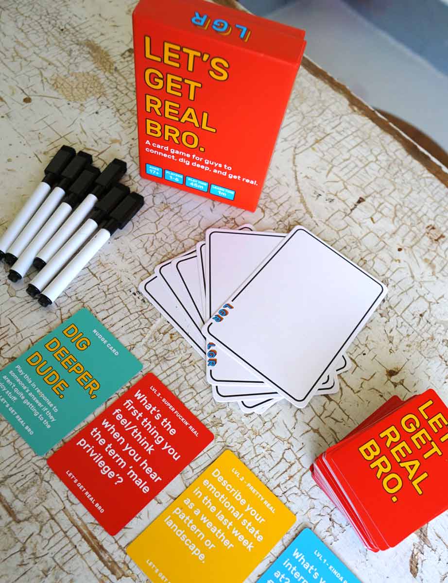 Box that says 'Let's Get Real Bro. A card game guys to connect, dig deep, and get real' and a number of cards and dry erase markers