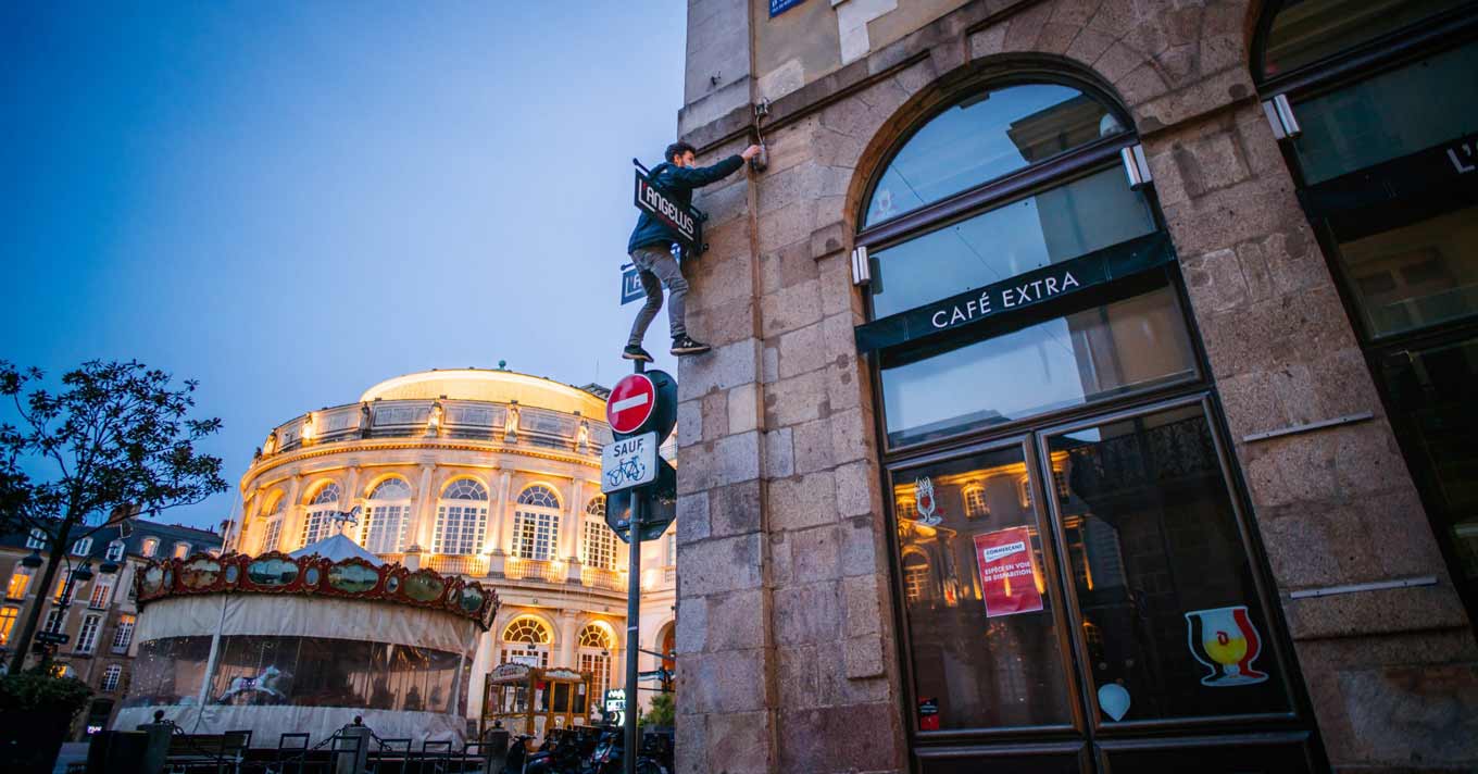 A parkour acrobat climbs a sign to flip a light switch on a building