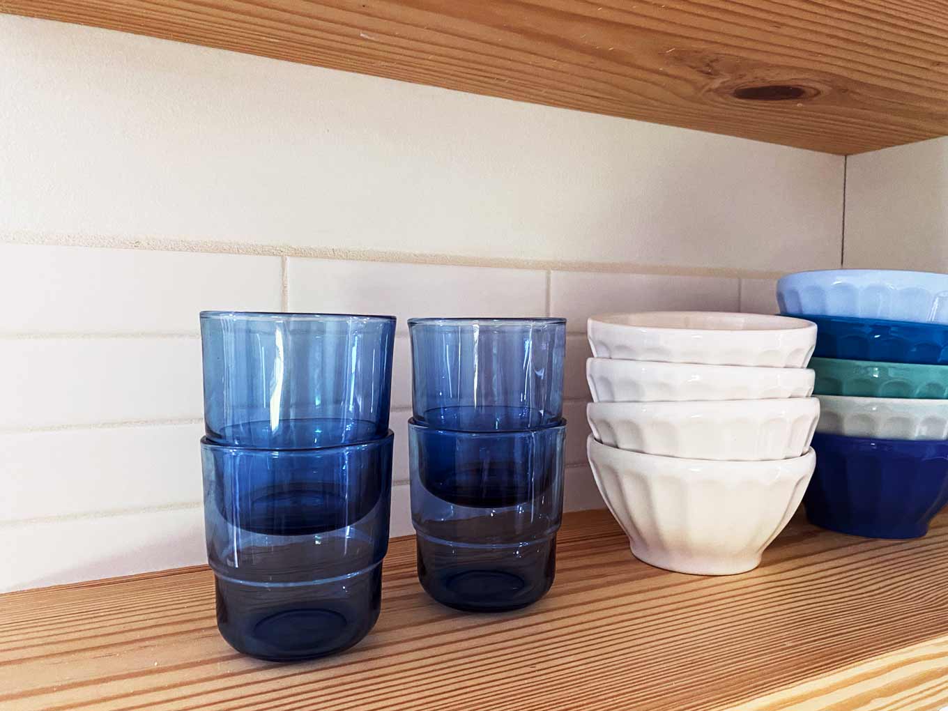 Small blue glasses, stacked on a shelf with small bowls
