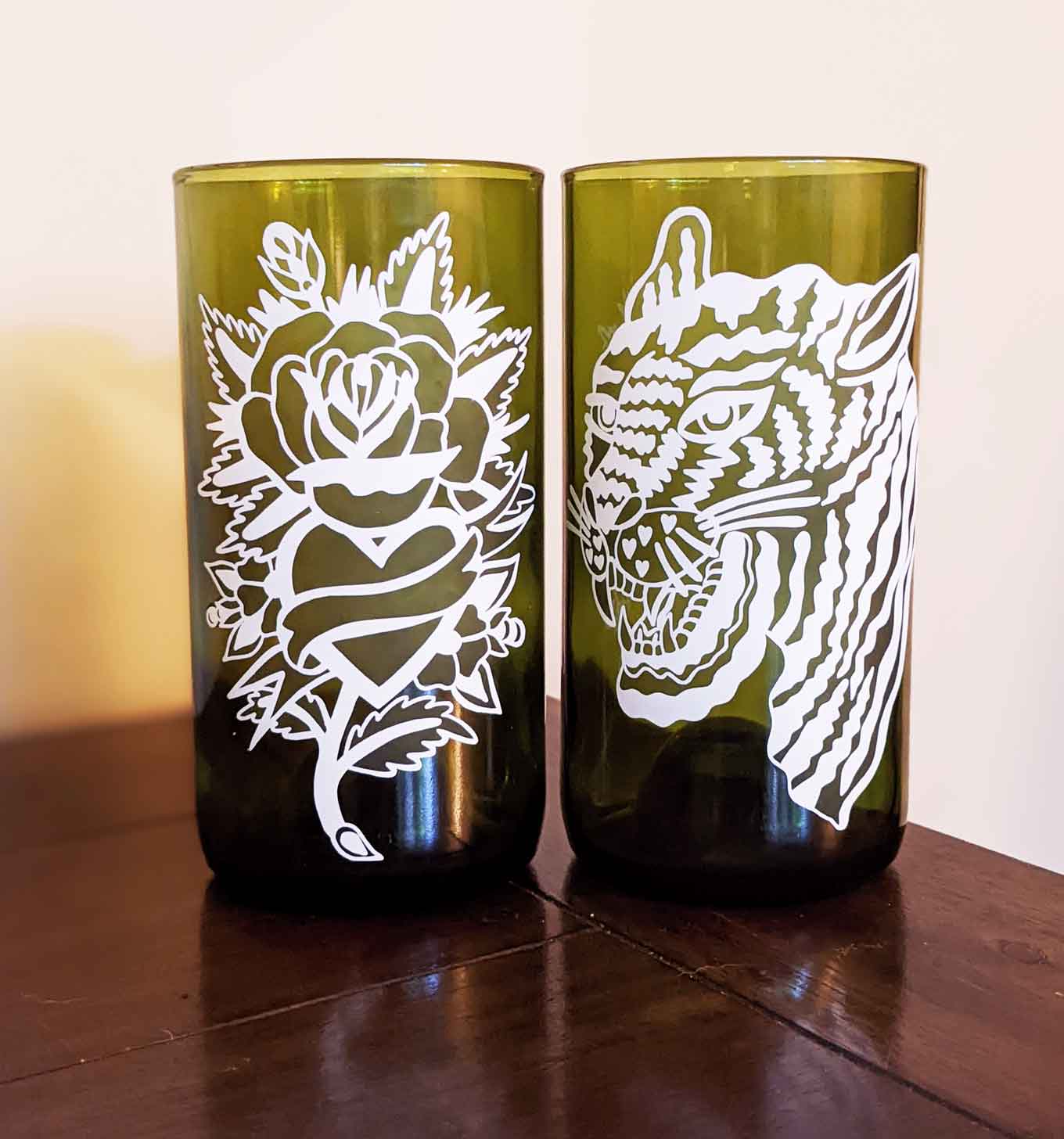 Two green recycled glasses, one with a flower design printed on it and other with a tiger design