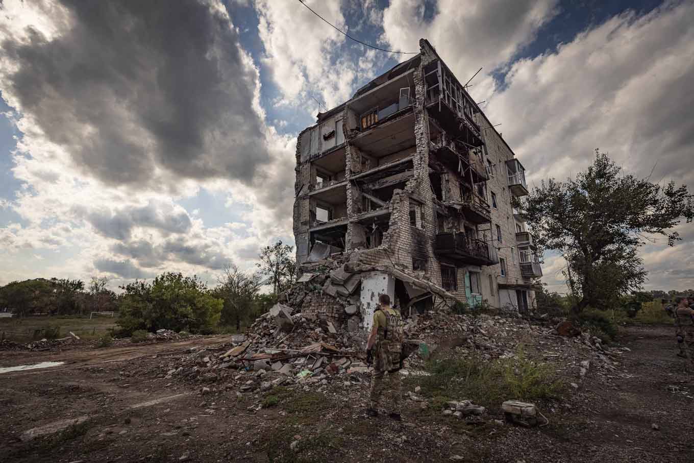 A member of the Ukrainian military stands in front of a destroyed apartment building