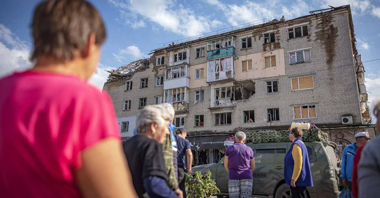 People stand outside of a destroyed apartment building in Ukraine