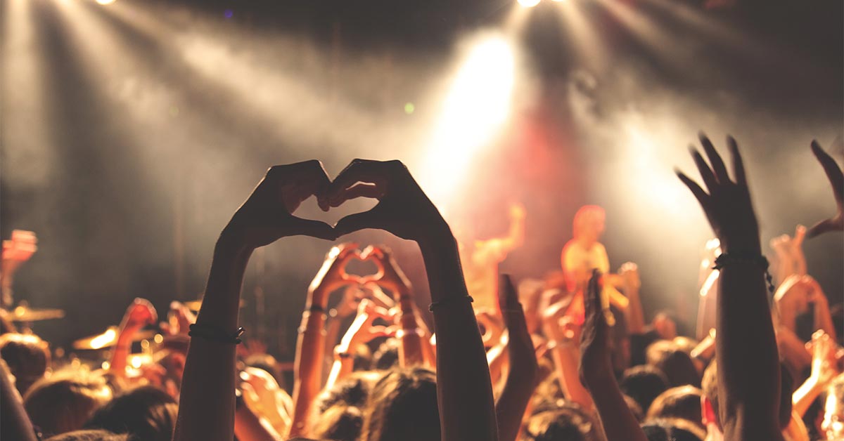 One fan in a concert makes a heart shape with their raised hands