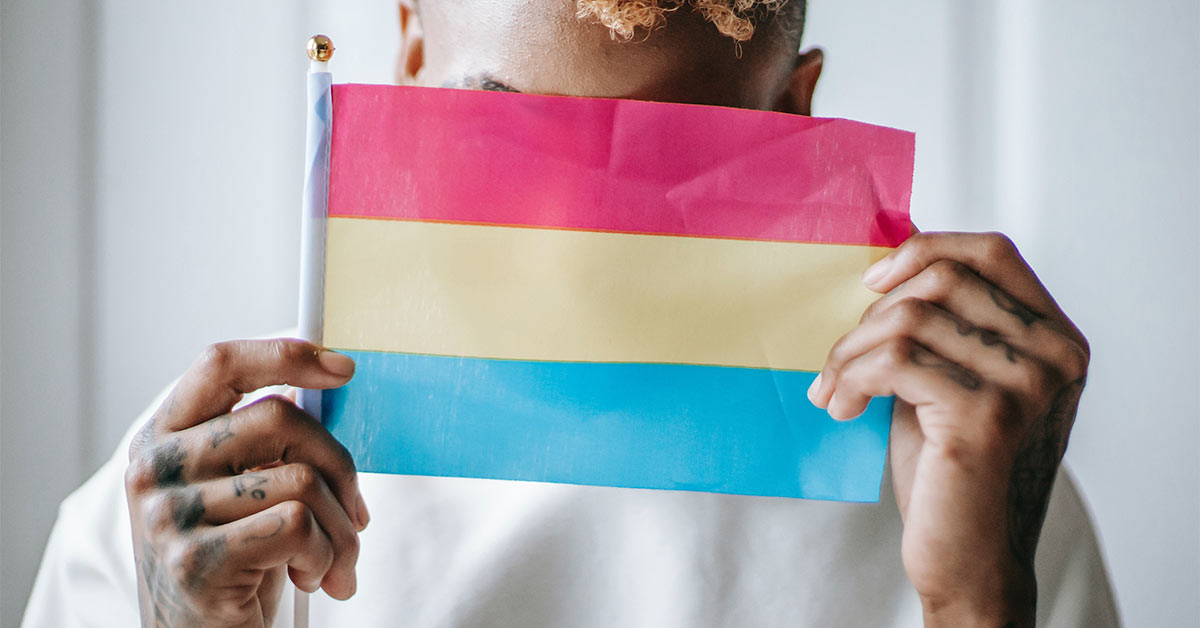 A person covers their face with a pansexual flag