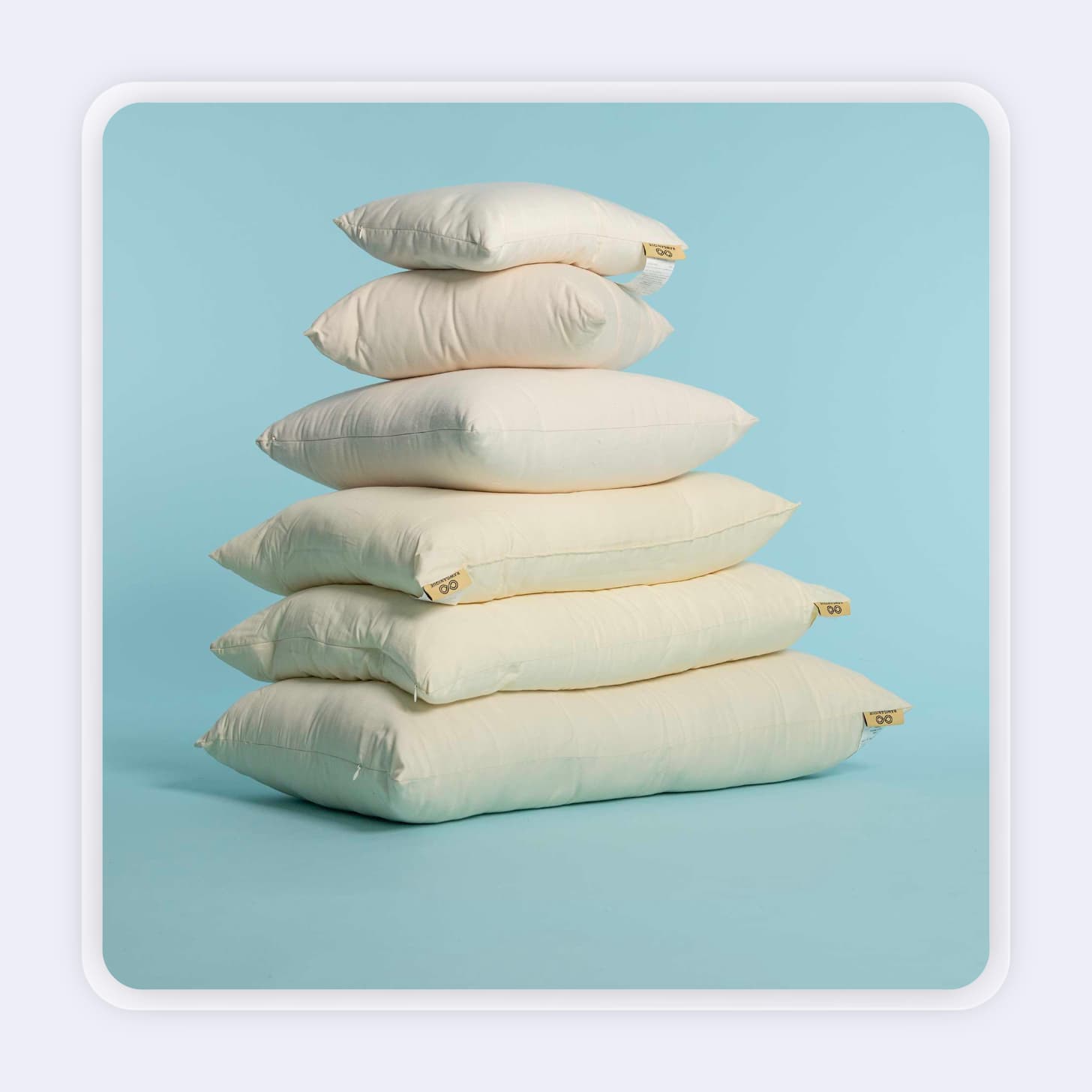 Six off-white pillows in varying sizes stacked on top of each other 