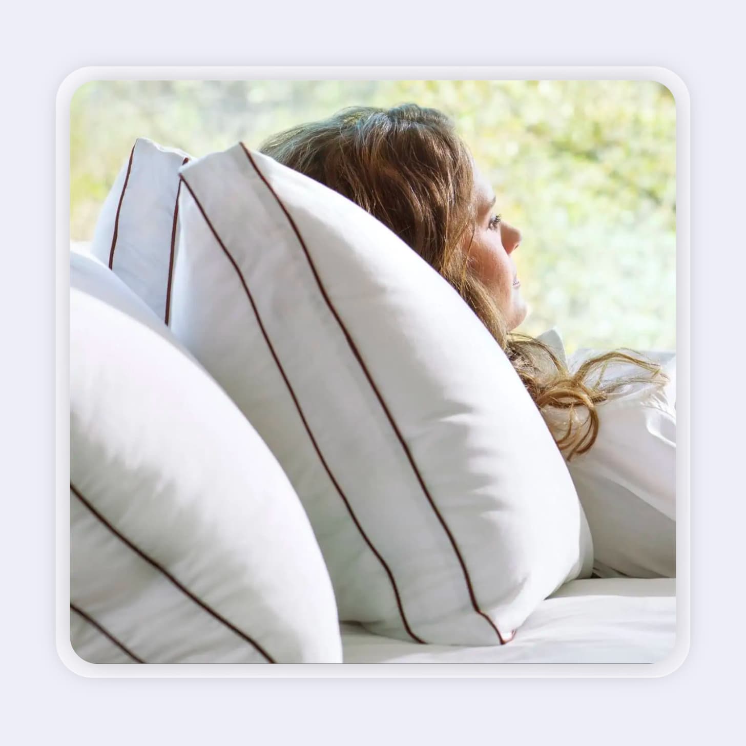 Woman laying against three pillows with a contrasting line around the seam of the pillows