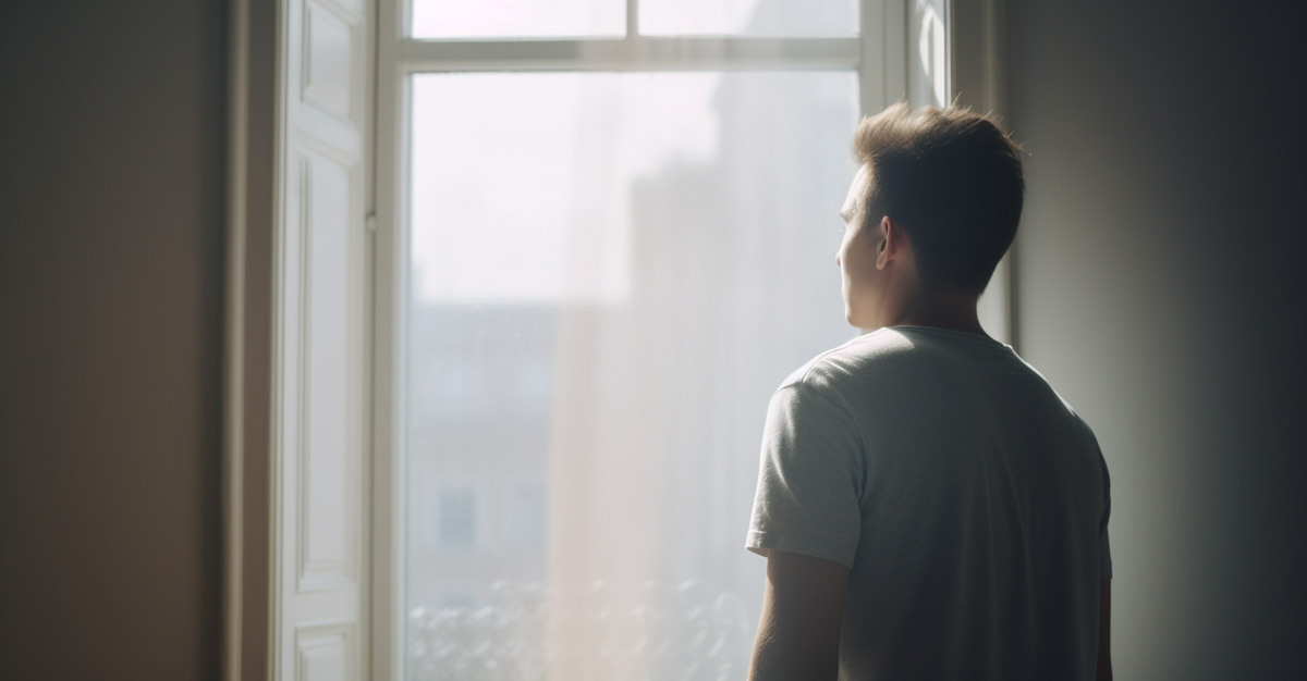 Photo of a man, viewed from behind, looking out a window while he says positive affirmations