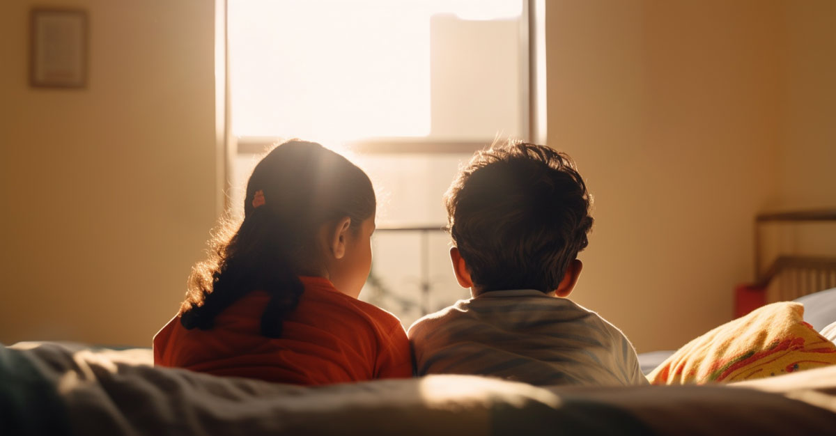 Two kids — a brother and sister — sit on a soft couch and look out the window while they practice their positive affirmations