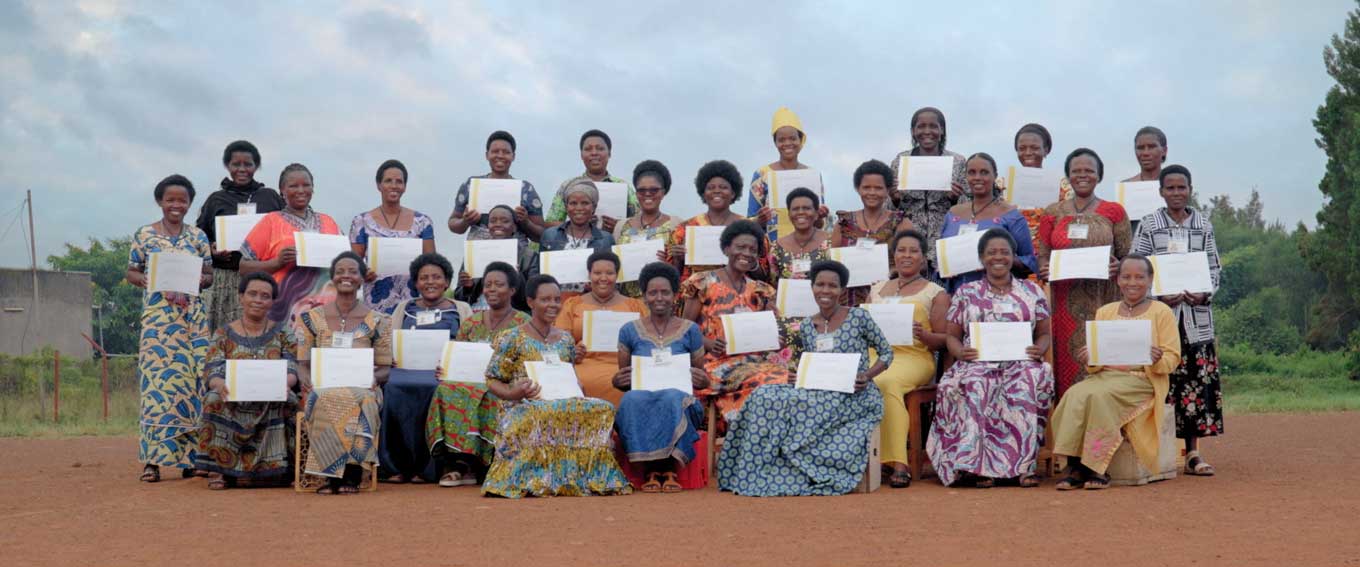 A group of African women in colorful dresses smile while holding up certificates. 
