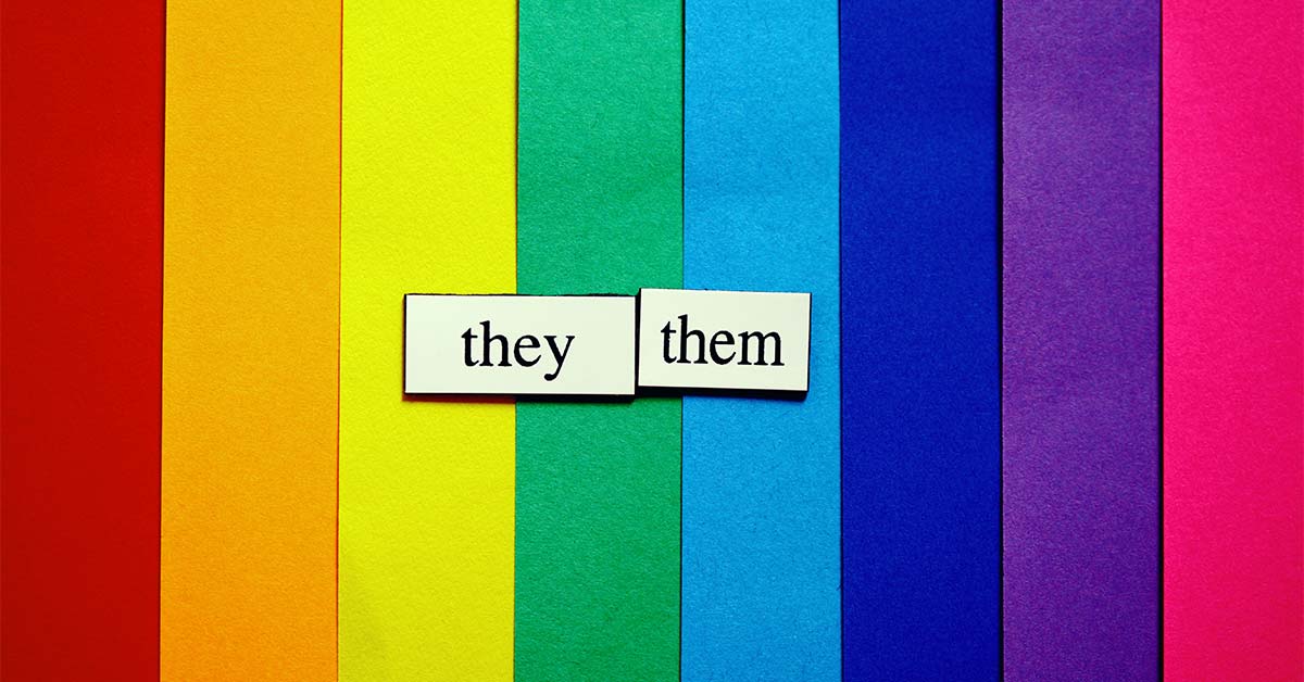 Paper cutouts with "They/them" pronouns written on top of a rainbow background