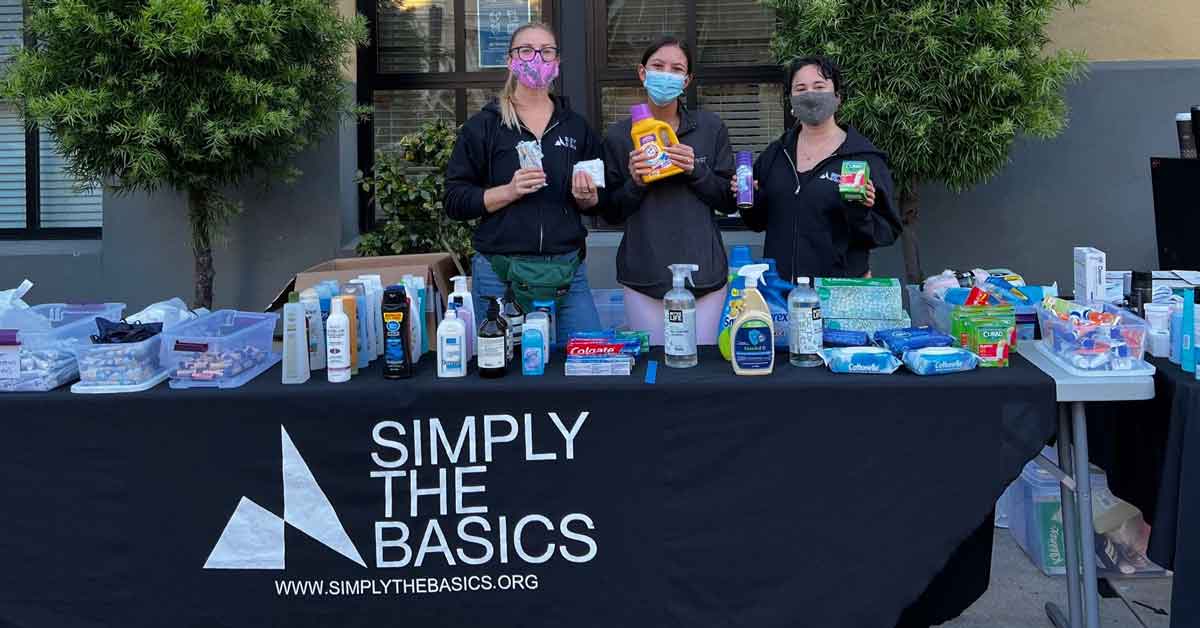 Three women stand behind a table holding up hygiene products