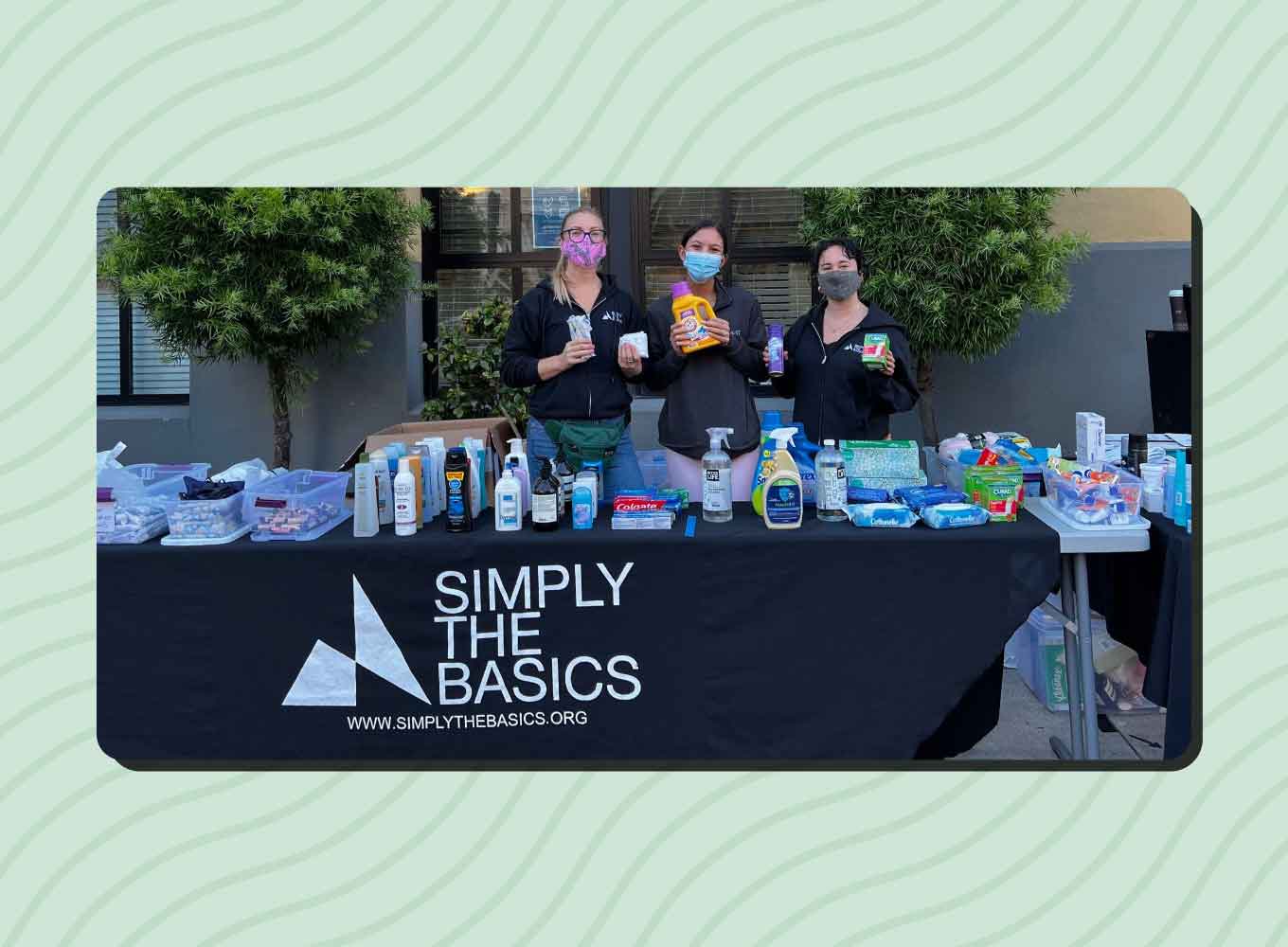 Three women stand behind a table holding up hygiene products