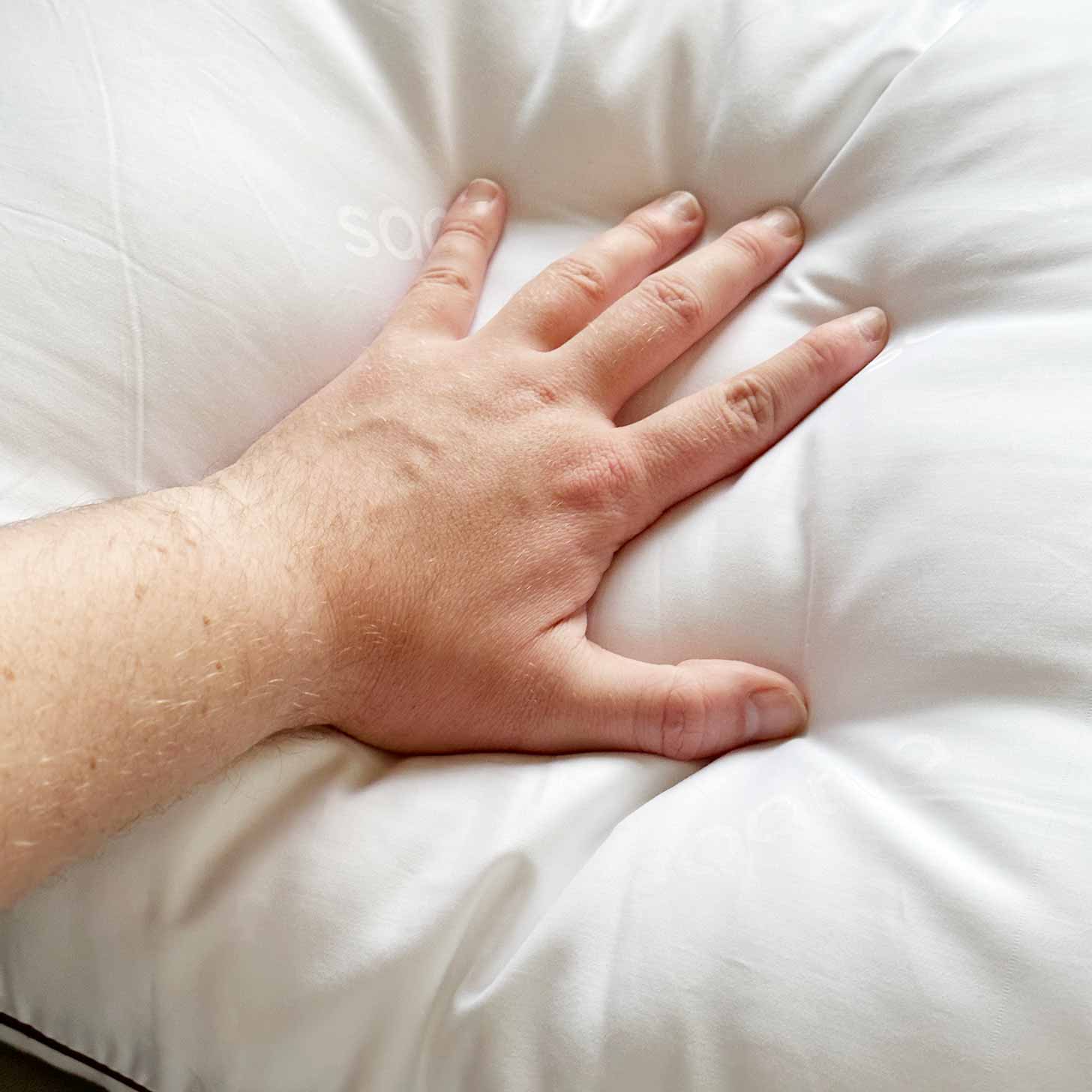 A hand pushing into Saatva pillows to show how soft yet firm they are