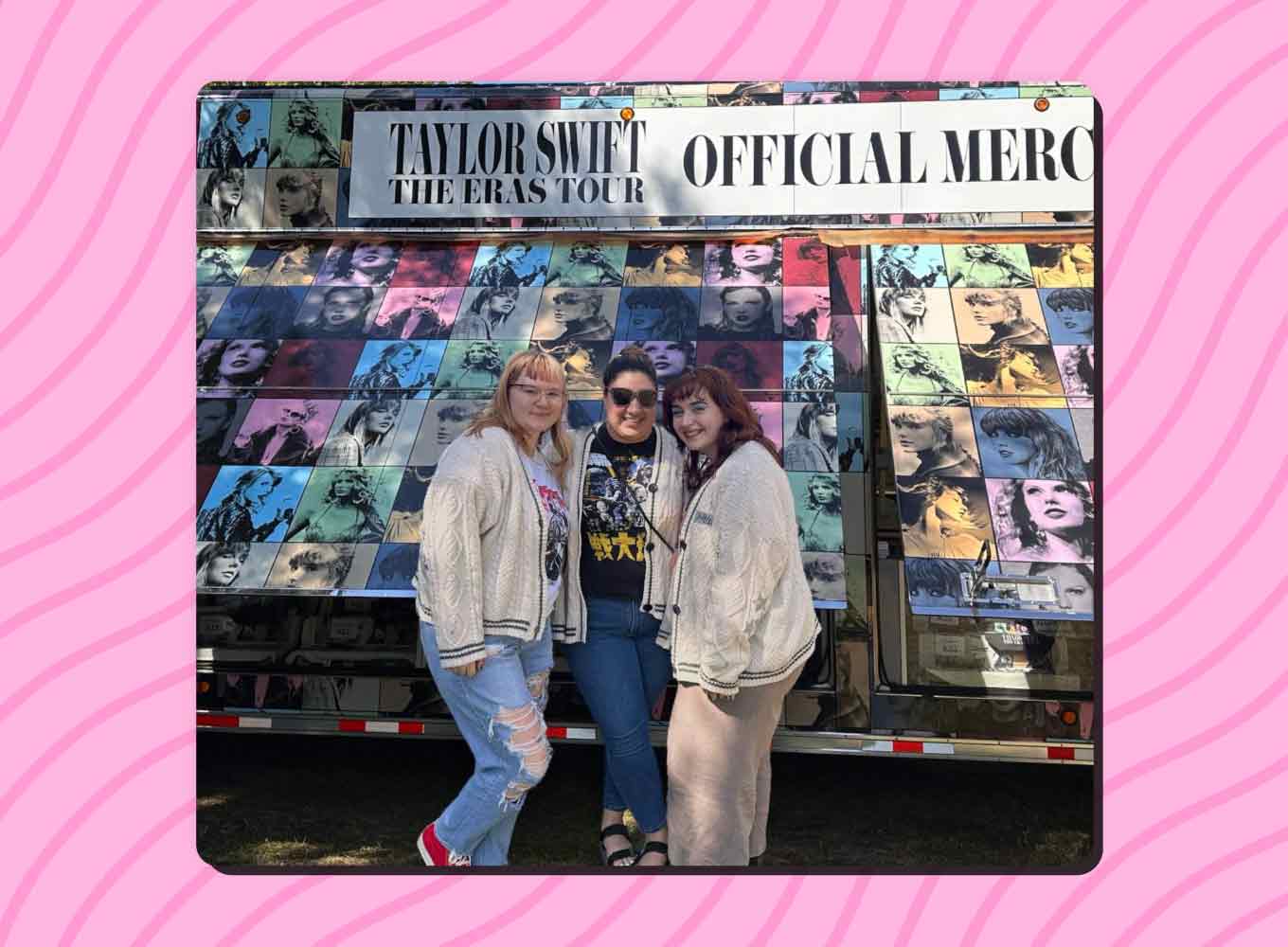Three women in cardigan sweaters stand outside of a Taylor Swift merch trailer.