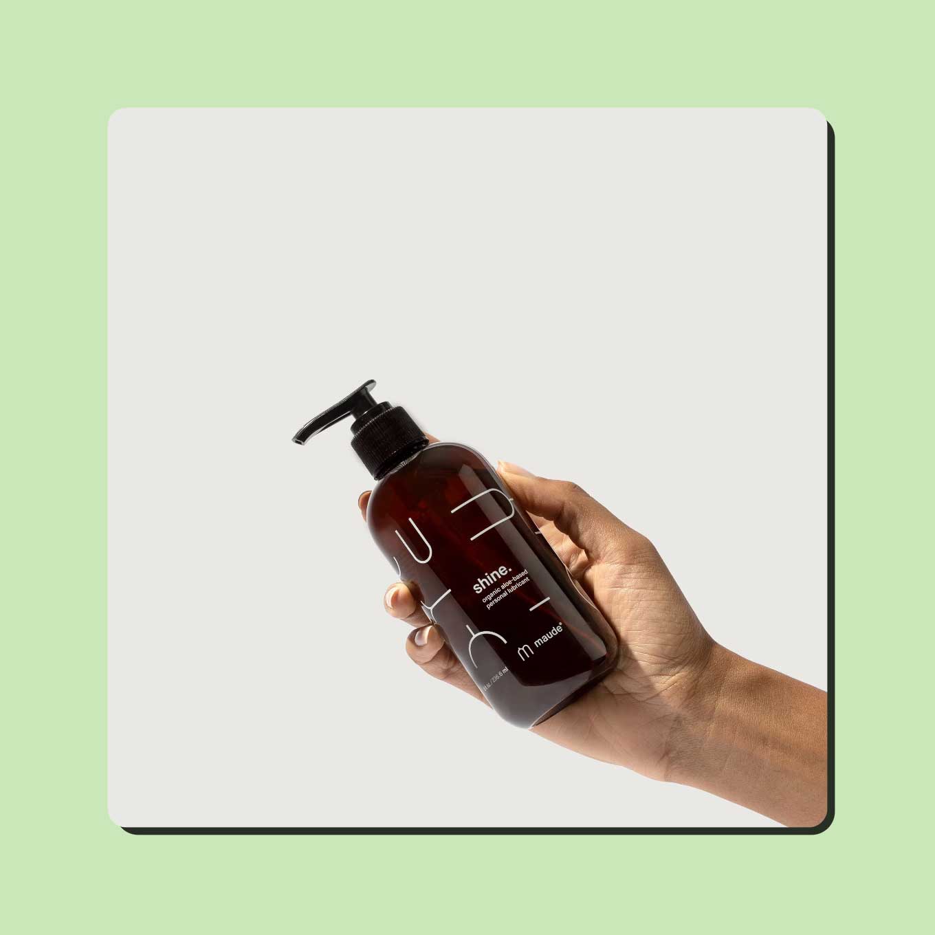 A hand holds up an amber bottle of Shine personal lubricant