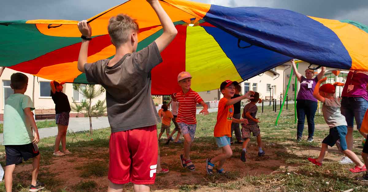 Children run around beneath a colorful parachute 