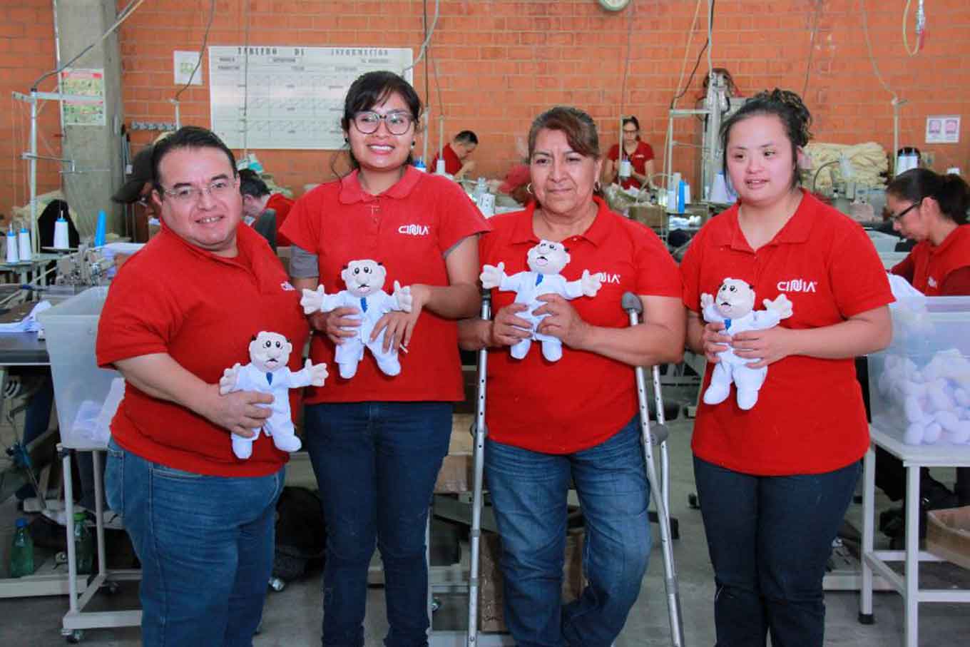 Four people hold Dr. Simi dolls in a factory