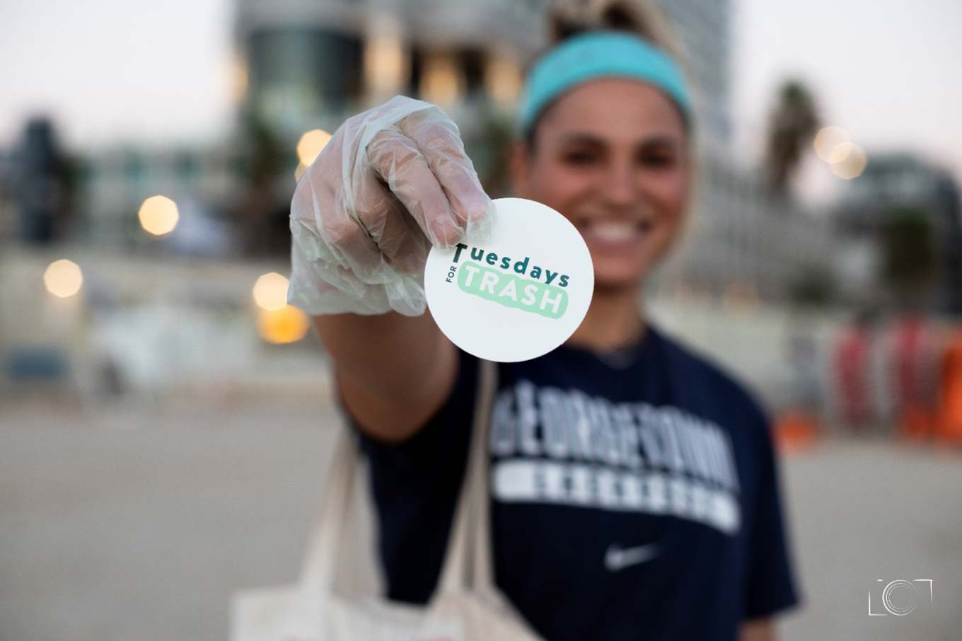 A girl holds up a Tuesdays for Trash sticker with a gloved hand.