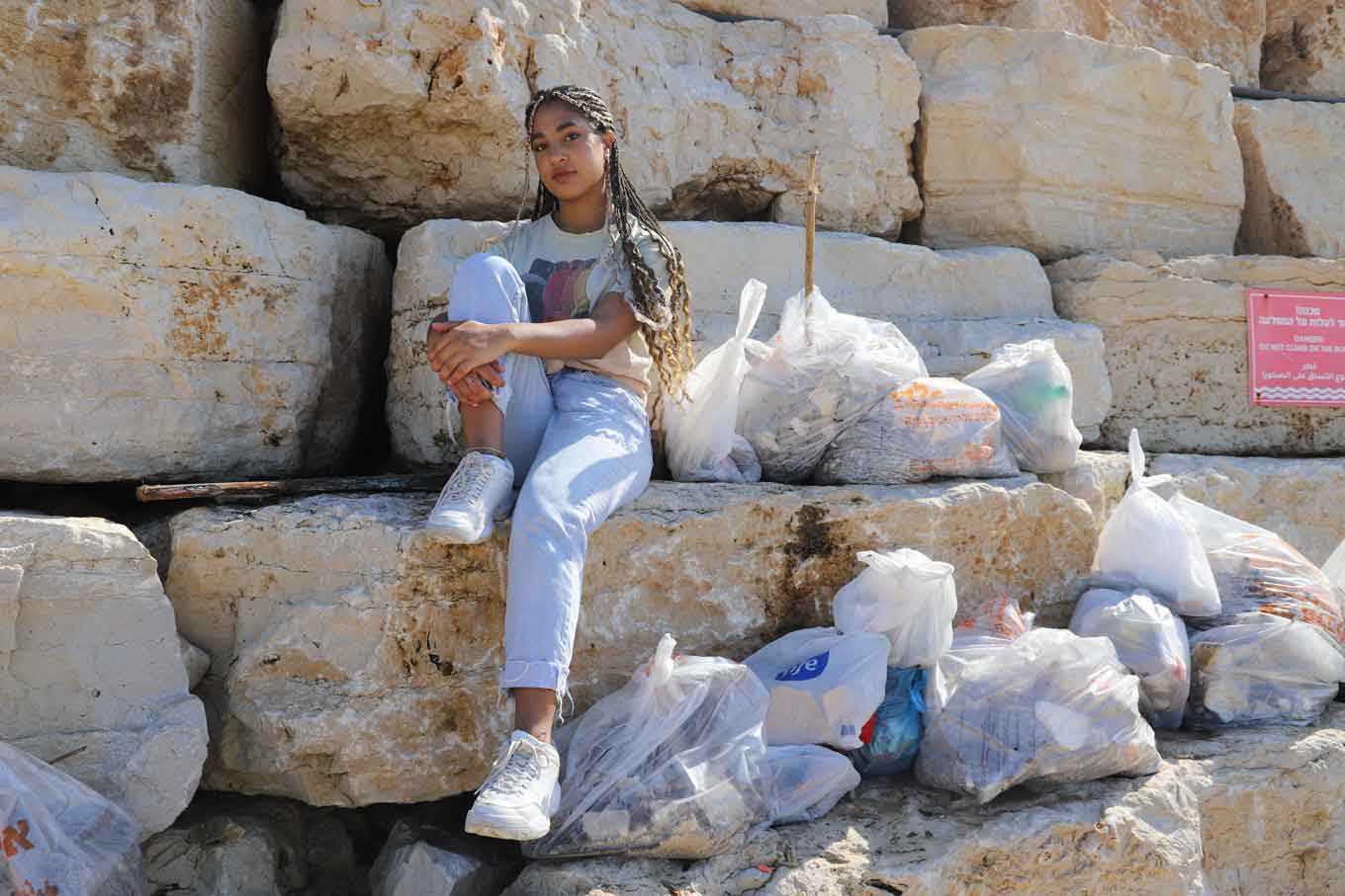 Sharona Shnayder sits on rocks, surrounded by bags of trash.